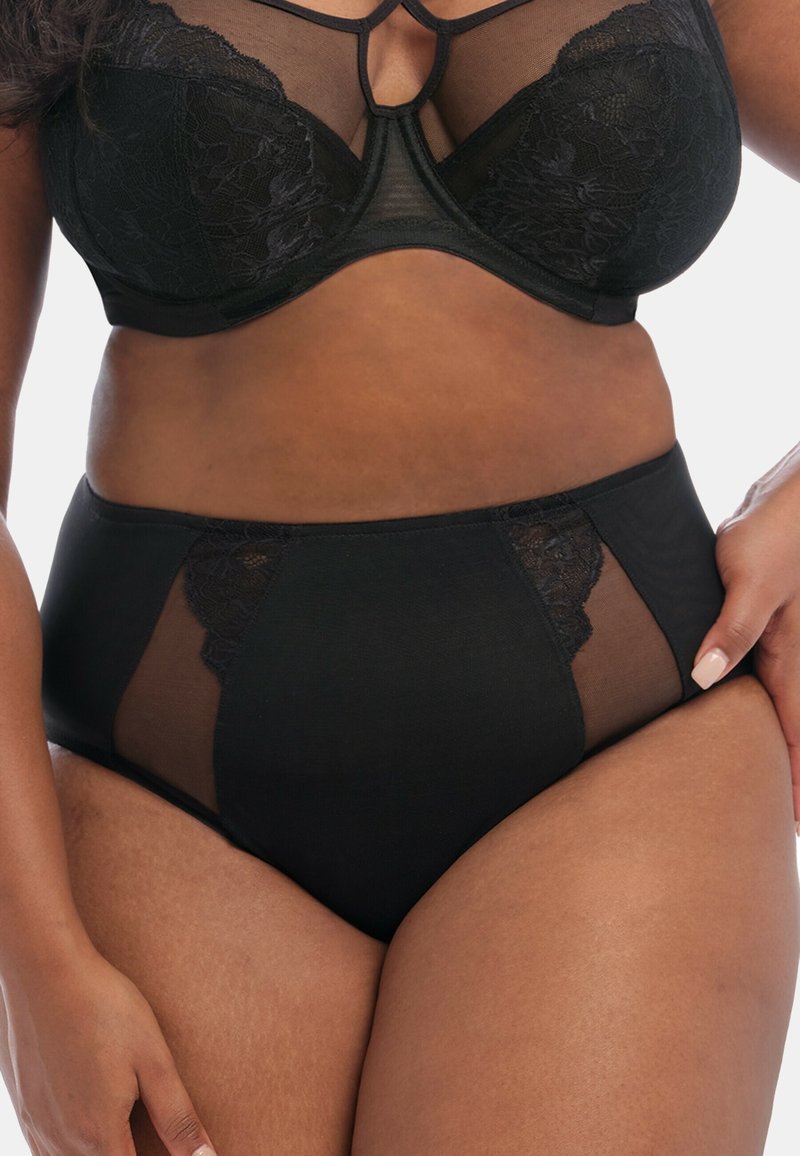 Ensemble de lingerie noire comprenant un soutien-gorge avec des accents en dentelle et armatures, ainsi que des culottes taille haute avec des panneaux en dentelle transparente. Fini en tissu lisse.