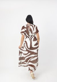 Braun-weißer, gemusterter Maxikleid mit kurzen Ärmeln, tailliertem Bund und einer Bindeschlaufe im Rücken. Aus glattem, leichtem Stoff.