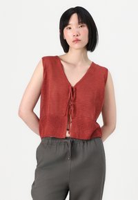 Rustfarget, cropped strikket topp med V-hals, frontknutdetalj og ribbet tekstur. Kombinert med løse grå bukser.