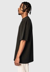 Black cotton oversized t-shirt with short sleeves, featuring a crew neckline and minimalistic front design. Model displayed in profile.