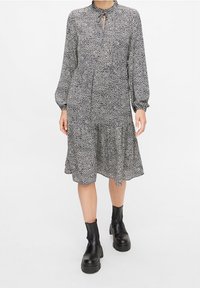 Vestido de manga larga en estampado floral en blanco y negro, con un cuello alto, detalle de abertura en la parte delantera y un volante en la parte inferior, combinado con botas negras.