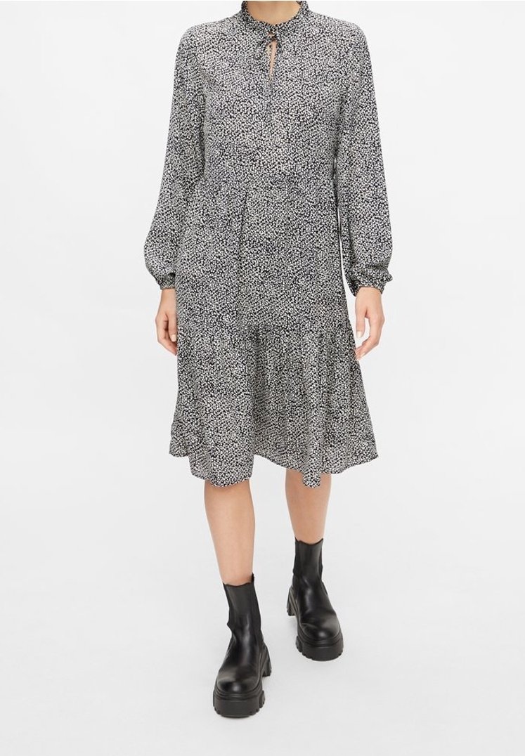 Vestido de manga larga en estampado floral en blanco y negro, con un cuello alto, detalle de abertura en la parte delantera y un volante en la parte inferior, combinado con botas negras.