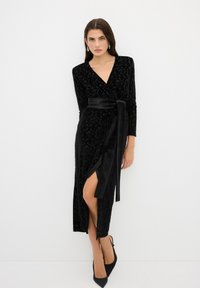 Schwarzes Samt-Wickelkleid mit langen Ärmeln, einem tiefen V-Ausschnitt und einem Satin-Gürtel. Verfügt über einen hohen Schlitz bis zum Oberschenkel und ein strukturiertes florales Muster.