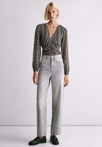 Svijetlosive hlače visokog struka uparene s dugim crnim bluzonskom s uzorkom, koja se chiffon vezuje i ima V-izrez i teksturiranu tkaninu. Crne cipele.