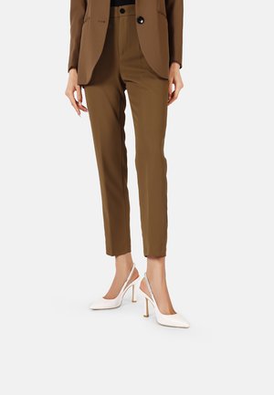 Pantaloni marroni su misura con finitura dall'effetto texture abbinati a décolleté bianchi slingback con punta affusolata e tacchi alti sottili.