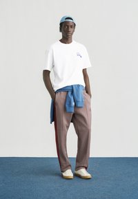 Λευκό μπλουζάκι με μπλε γραφικό στοιχείο, συνδυασμένο με κόκκινο και καρό παντελόνι. Επάνω φοράει στρωτό ανοιχτό μπλε πουλόβερ δεμένο στη μέση, και λευκά αθλητικά παπούτσια.