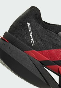 Black athletic shoe featuring a textured upper, red accents, sleek design, and a lightweight sole with a visible brand logo.