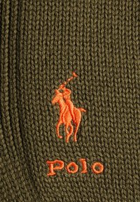 Tissu en maille vert olive avec un logo de joueur de polo brodé en orange et le texte « Polo » dans une teinte orange assortie.