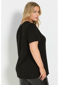 Camiseta negra de manga corta con un ajuste relajado, que presenta botones decorativos en los hombros y tejido suave para mayor comodidad.