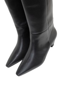 Czarne skórzane kozaki za kolano o gładkiej fakturze, zakończone szpiczastym noskiem i niskim, szerokim obcasem. Charakteryzują się dopasowanym krojem i bezszwową konstrukcją.