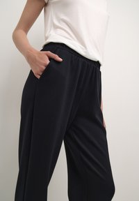 Zwarte, loszittende broek van zachte stof, met een elastische tailleband en zijzakken, gedragen met een wit T-shirt.