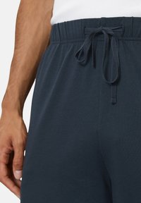 Navy blue sweatpants with a stretchy waistband, flat drawstring, and soft cotton fabric. Close-up view of waistband details.