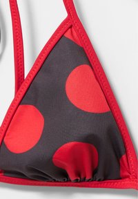 Haut de bikini triangle en tissu noir avec de gros pois rouges et surpiqûres rouges sur fond blanc.