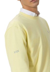 Sudadera de algodón amarilla con un cuello acanalado y detalle bordado en azul en la manga. Corte holgado, textura sutil con acabado suave.
