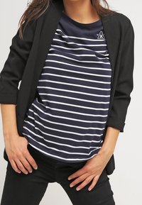 Woman wearing navy and white striped shirt under a black blazer with three-quarter sleeves, paired with black pants.