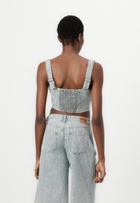 Light blue denim cropped top with wide shoulder straps, shirred back, and a textured surface. Paired with loose-fitting denim trousers.