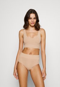 Nude-colored crop top and high-waisted briefs made from smooth fabric; features wide straps and an elastic band with subtle branding.