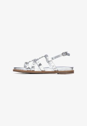 Sandalias metálicas plateadas con múltiples correas cruzadas, detalles de remaches, correa ajustable en el tobillo, suela plana y base color marrón claro.