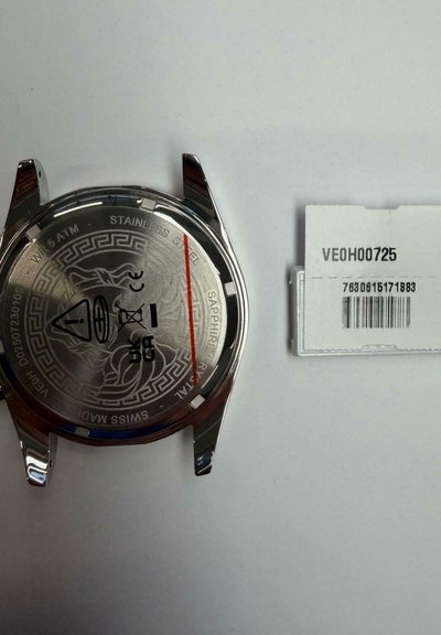 Roostevabast terasest kella korpuse tagakülg graveeritud disaini ja sertifitseerimismärkidega, kõrval valge ristkülikukujuline silt vöötkoodi ja koodiga VE0H00725.