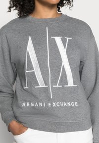 Grå sweatshirt med stort vitt "AX"-logotyp och texten "ARMANI EXCHANGE", tillverkad av mjukt bomullsmaterial med rundad halsdesign.