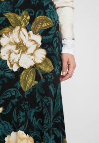 Blommig kjol med svart bakgrund och stora vita och guld blommor, gröna blad och intrikata teal-mönster. Slät tygtextur.