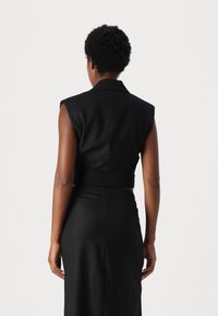 Svart, ermeløs cropped blazer med en strukturert krage og stripet mønster, kombinert med et matchende skjørt, sett bakfra.