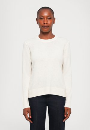 Long-sleeve cream sweater made of soft knit fabric, featuring a round neckline and ribbed cuffs and hem. Worn with dark denim pants.