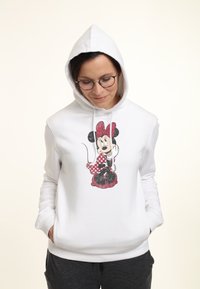 Vit hoodie med en grafik av en tecknad figur med en röd prickig rosett. Mjuk tyg med avslappnad passform och framfickor.