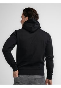 Sudadera negra con cuello alto y cordón ajustable. Presenta mangas largas y puños acanalados, está confeccionada en una suave tela texturizada.