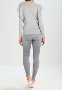 Maglione grigio con schiena arricciata, design aderente; abbinato a leggings grigio chiaro e sneaker rosa tenue. Tessuto liscio, caratteristiche semplici.