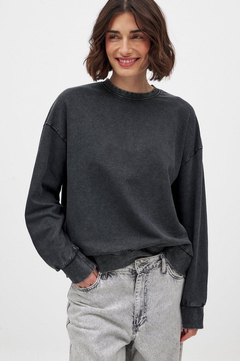 Grijze sweatshirt met een ontspannen pasvorm, ronde hals en geribbelde manchetten. Gecombineerd met lichtgrijze high-waisted jeans. Zachte stoftextuur.