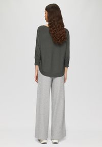 Dunkelgrauer oversized Pullover mit langen Ärmeln, kombiniert mit weit geschnittenen, hellgrauen karierten Hosen und weißen Sneakers.
