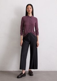 Chemise boutonnée bordeaux avec un motif floral, associée à un pantalon noir à jambes larges et des chaussures noires à enfiler, sur un fond neutre.