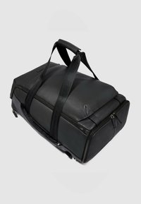 Zwarte leren reistas met dubbele ritssluitingen, gestructureerd oppervlak en brede schouderbanden. Heeft een rechthoekige vorm met schuine hoeken.