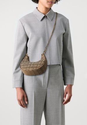 Femme portant un costume à carreaux noir et blanc avec un sac à bandoulière en forme de croissant marron à motifs, doté d'une chaîne dorée.