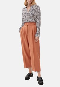 Kwiatowa bluzka z długim rękawem w kolorach granatowym, białym i różowym, zestawiona z wysokim stanem i szerokimi nogawkami w kolorze rdzawym. Grube czarne mokasyny.