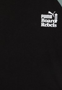 Czarna koszulka z miękkiej bawełny, z białym logo "PUMA Board Rebels" oraz małą grafiką pumy. Prosty design z krótkimi rękawami.