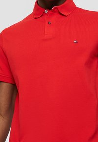Chemise polo rouge en tissu texturé, dotée d'une patte de boutonnage à deux boutons et d'un petit logo de marque sur la poitrine gauche.