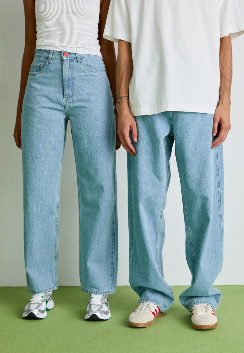 Jean taille haute bleu clair avec une coupe décontractée, associé à un haut en maille blanche et un t-shirt blanc oversized. Des baskets décontractées complètent le look.