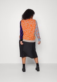 Colorful knit sweater featuring orange leopard print, blue and purple stripes, and a ribbed hem. Paired with a black knee-length skirt.