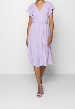 Levandulové šaty délky ke kolenům s krátkými volánkovými rukávy, výstřihem do V a elastickým pasem; doplněné o kožené sandály na podpatku se zapínáním na pásky ve stejném odstínu.