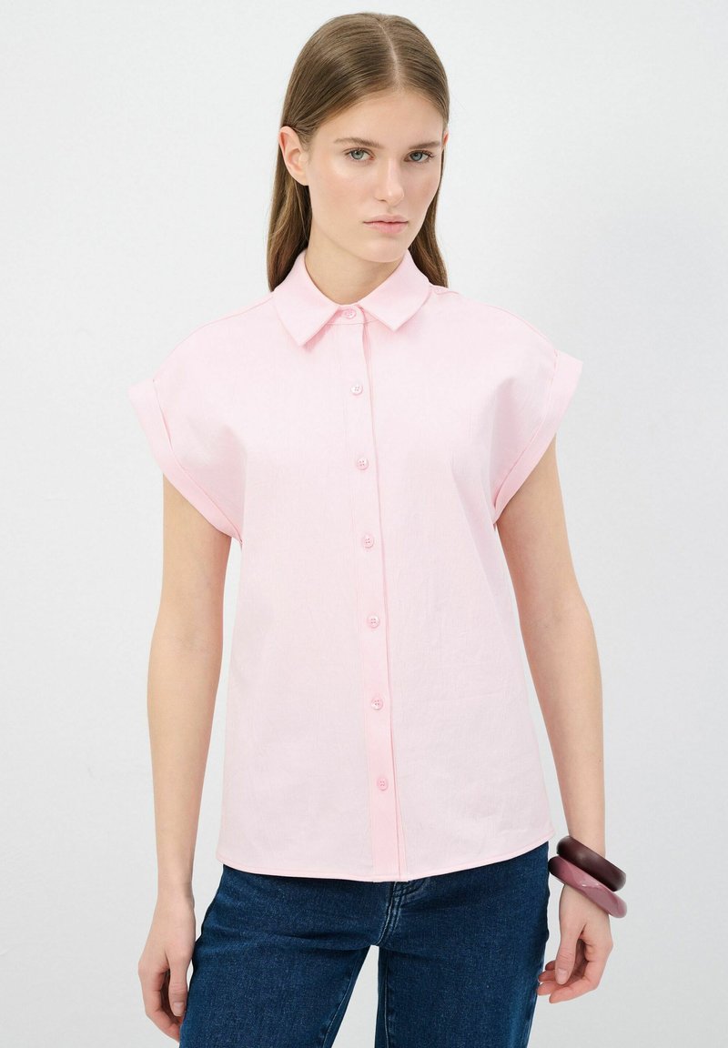 Camicia rosa chiaro a maniche corte con bottoni sul davanti, dotata di un colletto classico e una vestibilità comoda, abbinata a jeans blu scuro.