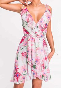 Květinové šaty vyrobené z lehké tkaniny, s růžovými a zelenými květinovými vzory, hlubokým výstřihem do V, nařasenými akcenty a detailem se zavázaným pasem.