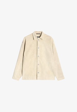 Beige manchetjakke i kordfløjl med knapper foran, spidst krave og lange ærmer. Glat tekstur og subtil glans.