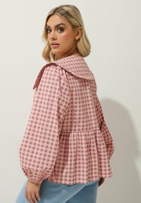 Rosa och vit gingham blus med en stor krage, puffärmar och peplummidja. Tillverkad av ett lätt, texturerat tyg.