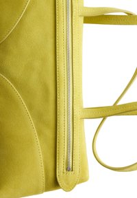 Bolso de ante amarillo con una cremallera plateada vertical y dos tirantes finos para el hombro sobre un fondo blanco.