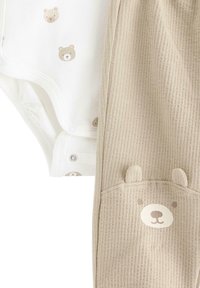 Katoenen romper met berenafdruk op een witte achtergrond, gecombineerd met geribbelde beige broek met een berengezicht en oren op de zak.