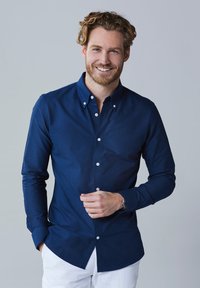 Marineblauwe button-up shirt gemaakt van gladde stof, met lange mouwen, een kraag en witte knopen, gecombineerd met witte broek.
