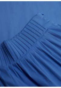 Tessuto blu a pieghe con una texture liscia. Il design presenta pieghe verticali e una tonalità di blu uniforme in tutto il tessuto.