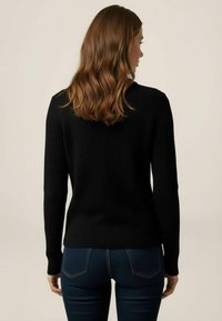 Pulover negru din tricot cu striații, mâneci lungi, decolteu rotund și croi mulat, purtat împreună cu blugi slim-fit de culoare albastru închis.